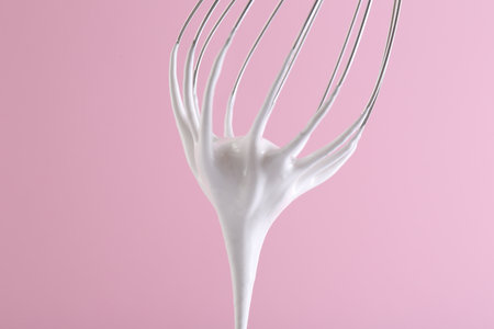 Whisk with whipped cream on pink background, closeup