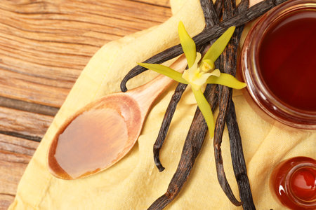 Aromatic vanilla extract, pods and flower on wooden table, top view