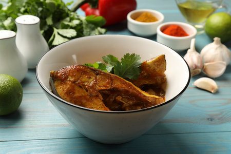 Tasty fish curry and ingredients on light blue wooden table, closeup. Indian cuisine