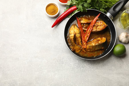 Tasty fish curry in frying pan and ingredients on light gray table, flat lay. Space for text. Indian cuisineの写真素材
