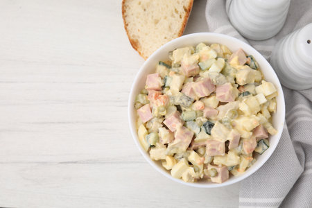 Tasty Olivier salad with boiled sausage in bowl on white wooden table, top view. Space for textの写真素材