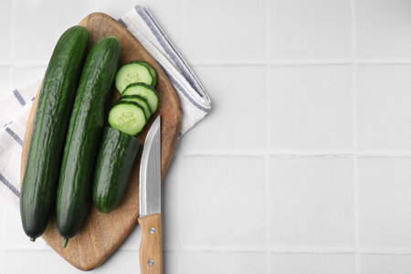 Fresh cucumbers and knife on white tiled table, top view. Space for textの写真素材