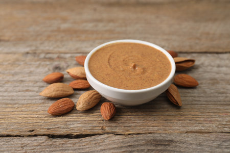 Delicious nut butter in bowl and almonds on wooden table, closeupの写真素材