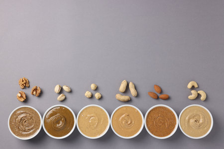 Many tasty nut butters in bowls and nuts on gray table, flat lay. Space for textの写真素材