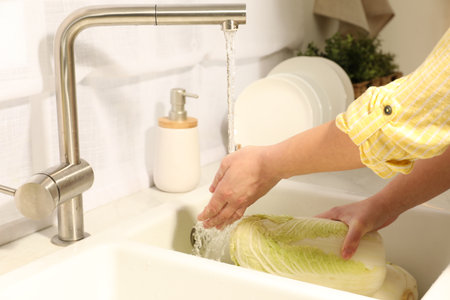 Woman washing fresh Chinese cabbage under tap water in kitchen sink, closeupの写真素材