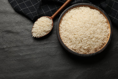 Raw basmati rice in bowl and spoon on black table, top view. Space for textの写真素材