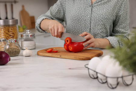 Cooking process. Woman cutting bell pepper at white countertop in kitchen, closeupの写真素材