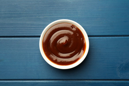 Tasty barbeque sauce in bowl on blue wooden table, top viewの写真素材