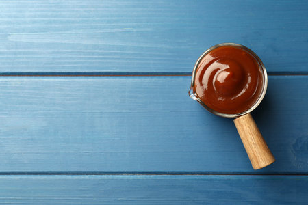 Tasty barbeque sauce on blue wooden table, top view. Space for textの写真素材