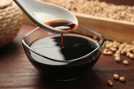 Taking soy sauce with spoon from bowl at wooden table, closeupの写真素材