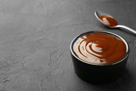 Tasty barbeque sauce in bowl on dark textured table, closeup. Space for textの写真素材
