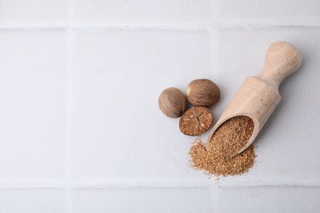 Scoop with gratified nutmeg and seeds on white tiled table, flat lay. Space for textの写真素材