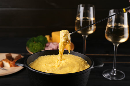 Dipping piece of ham into fondue pot with melted cheese on table, closeupの写真素材
