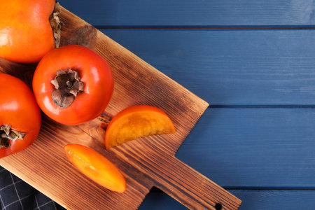 Delicious ripe persimmons on blue wooden table, top view. Space for textの写真素材