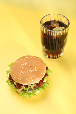 Burger with delicious patty and soda drink on yellow backgroundの写真素材