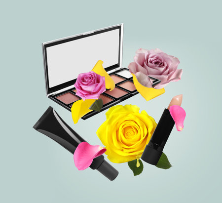 Different makeup products and beautiful roses in air on light greyish blue backgroundの写真素材