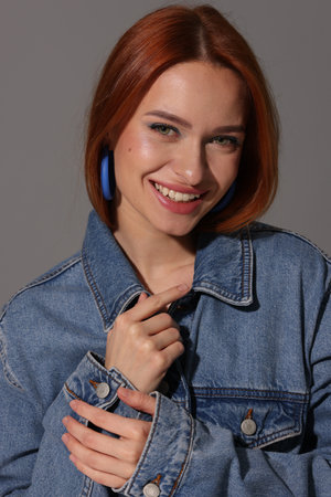 Beautiful young woman in denim jacket on gray background