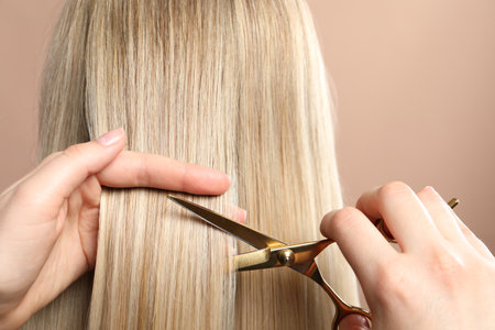 Hairdresser cutting client's hair with scissors on beige background, closeupの写真素材