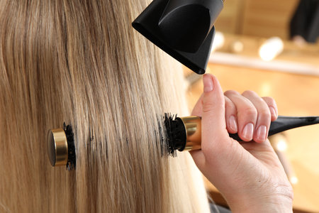 Hairdresser blow drying client's hair in salon, closeupの写真素材