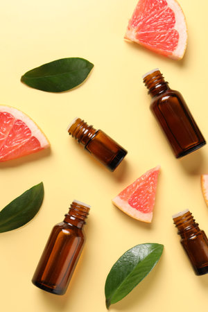 Grapefruit essential oil in bottles, leaves and cut fruit on yellow table, flat layの写真素材