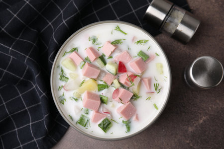 Delicious cold summer soup (okroshka) with boiled sausage in bowl on brown table, top viewの写真素材