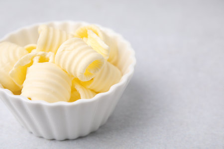 Tasty butter curls in bowl on light gray table, closeup. Space for text