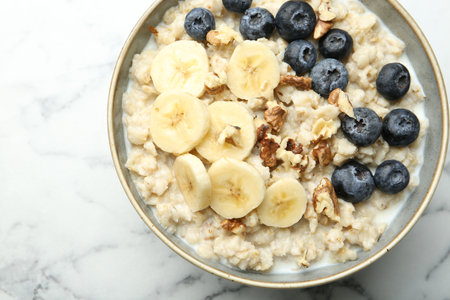 Tasty oatmeal with banana, blueberries, walnuts and milk served in bowl on white marble table, top viewの写真素材