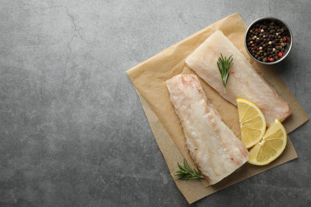 Fresh raw cod fillets, spices and lemon slices on gray table, flat lay. Space for text