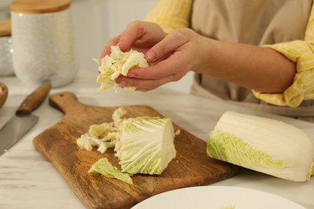 Woman with cut Chinese cabbage at white kitchen table, closeupの写真素材