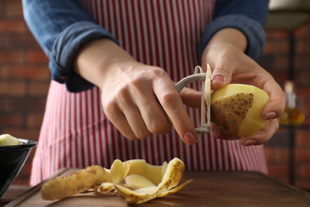 Woman peeling fresh potato at table indoors, closeup