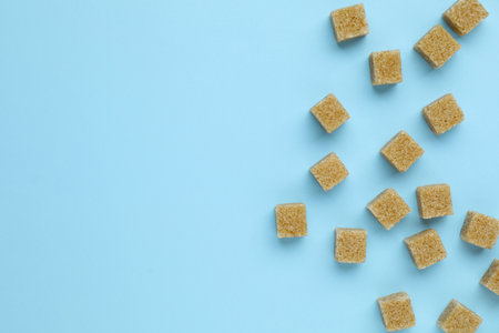 Brown sugar cubes on light blue background, flat lay. Space for text