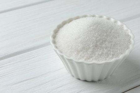 Granulated sugar in bowl on white wooden table, closeup. Space for textの写真素材