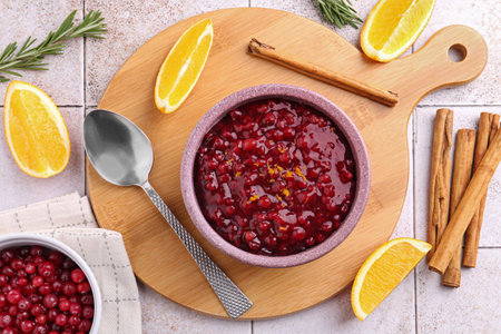 Tasty cranberry sauce in bowl and ingredients on white tiled table, flat layの写真素材