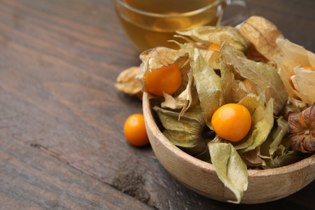 Ripe physalis fruits with calyxes in bowl on wooden table, closeup. Space for textの写真素材