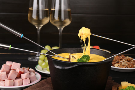 Dipping different products into fondue pot with melted cheese on table, closeupの写真素材