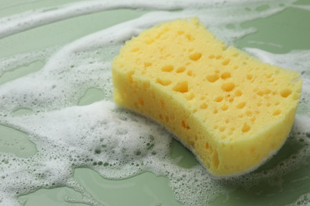 Yellow sponge with foam on green background, closeupの写真素材