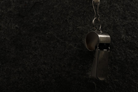 Referee equipment. Metal whistle on black textured background, closeup and space for textの写真素材