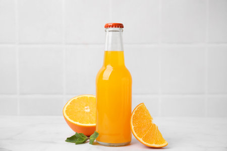 Delicious kombucha in glass bottle, orange and mint on white table