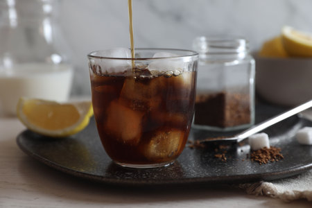 Pouring coffee into glass with ice cubes at white wooden table, closeup