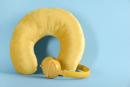 Yellow travel pillow and headphones on light blue background, space for textの写真素材