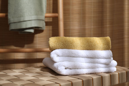 Stacked soft towels on wicker bench indoors, space for textの写真素材