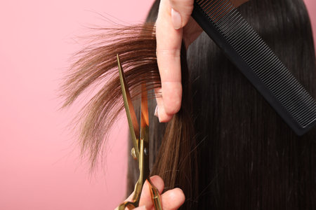 Hairdresser cutting client's hair with scissors on pink background, closeupの写真素材