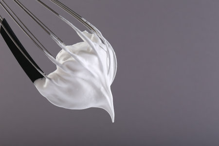 Whisk with whipped cream on gray background, closeup. Space for textの写真素材