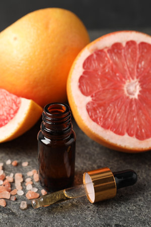 Grapefruit essential oil in bottle, pipette, sea salt and fruits on dark textured table, closeupの写真素材