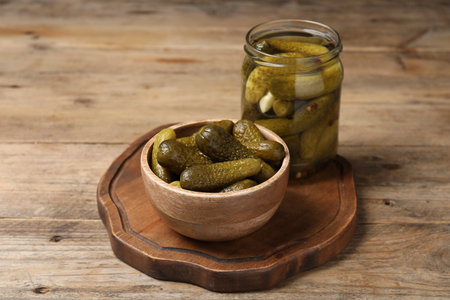 Tasty pickled cucumbers in jar and bowl on wooden tableの写真素材