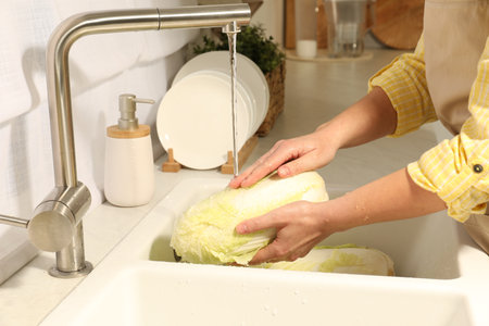 Woman washing fresh Chinese cabbage under tap water in kitchen sink, closeupの写真素材