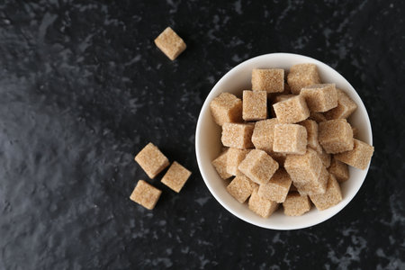 Brown sugar cubes in bowl on dark textured table, top view. Space for textの写真素材