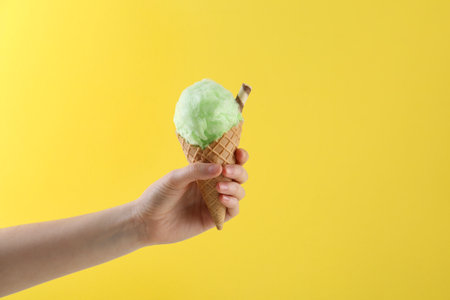 Woman holding waffle cone with cotton candy on yellow background, closeupの写真素材