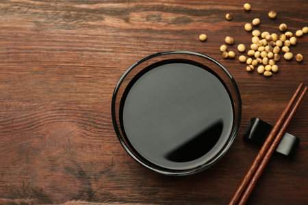 Soy sauce in bowl, soybeans and chopsticks on wooden table, flat lay. Space for textの写真素材
