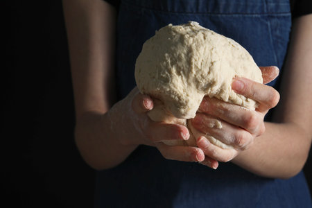 Making bread. Woman holding dough on dark background, closeup. Space for textの写真素材
